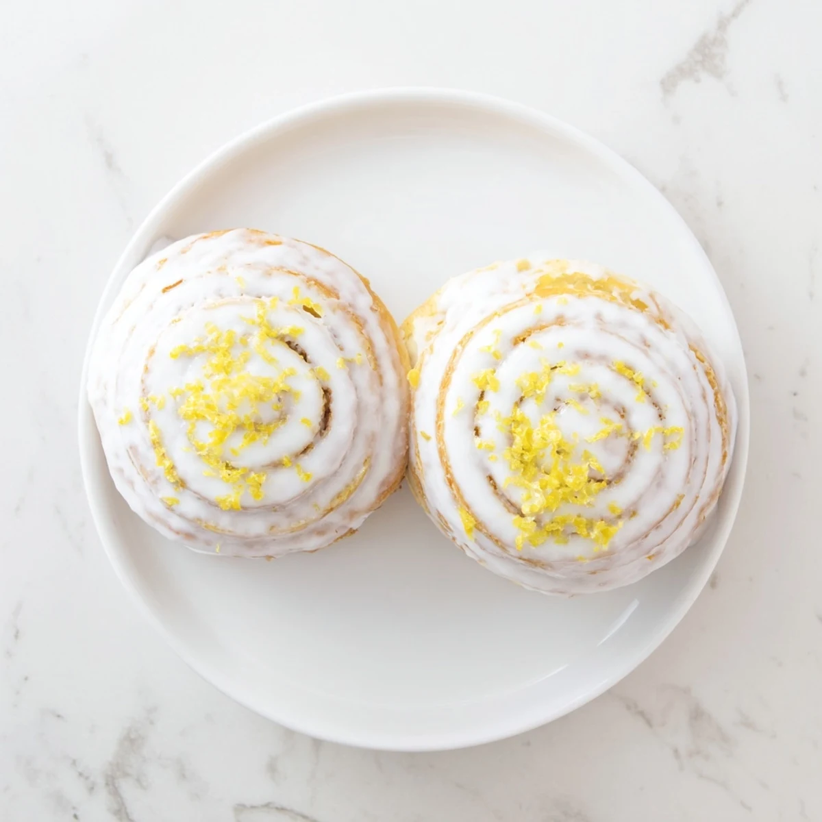Freshly baked lemon rolls drizzled with tangy glaze on a white serving plate