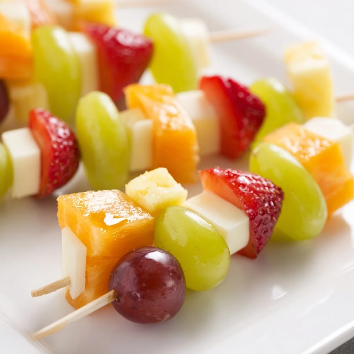 Colorful fruit and cheese kabobs arranged on a platter with grapes strawberries and cheddar cubes