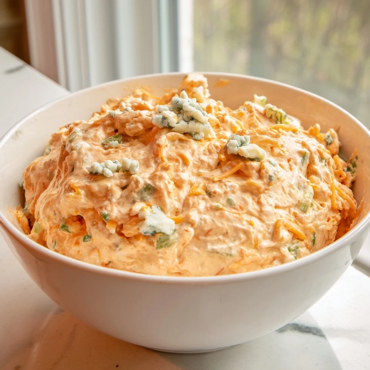 Creamy buffalo pickle dip served in a bowl with crisp veggie sticks and chips nearby