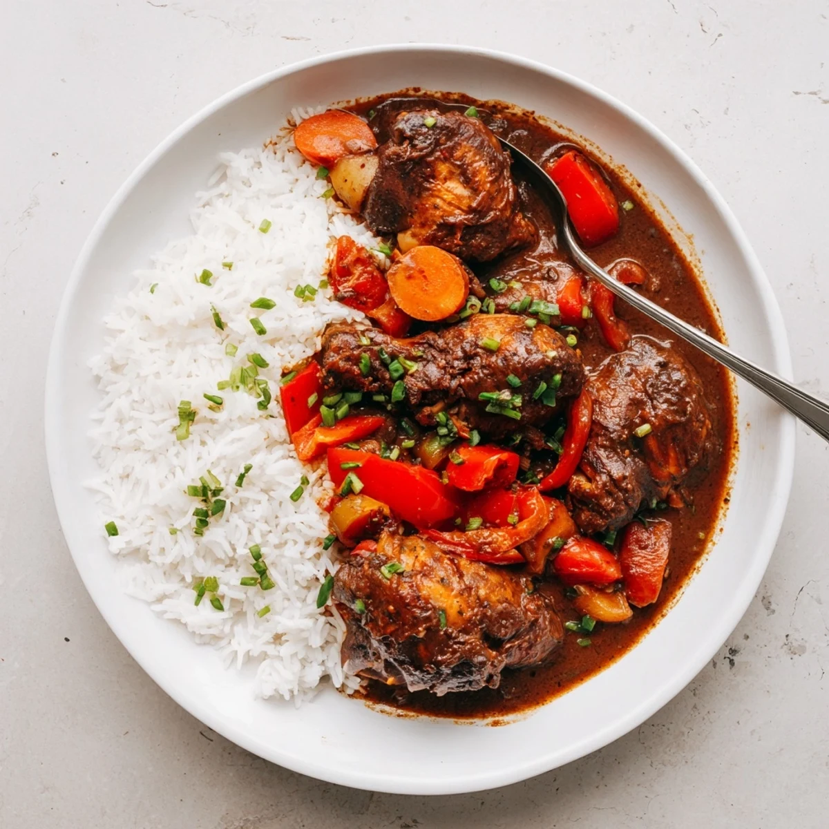 Golden seared Jamaican brown stew chicken served over steamed white rice with thick savory sauce ladled on top