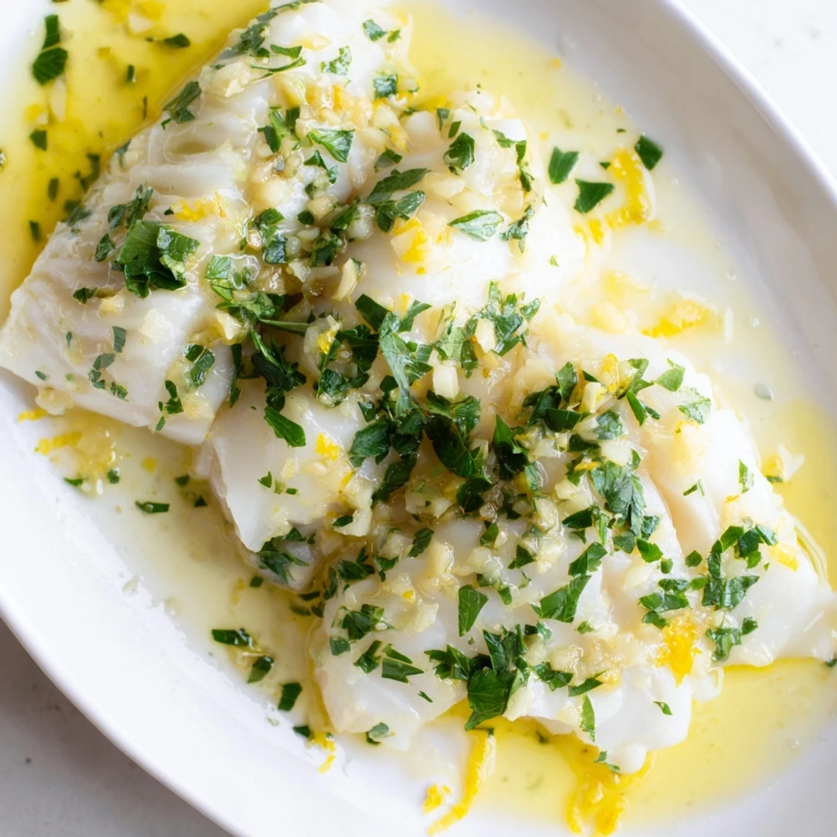 Flaky white cod fillets swimming in rich buttery lemon garlic sauce with lemon wedge