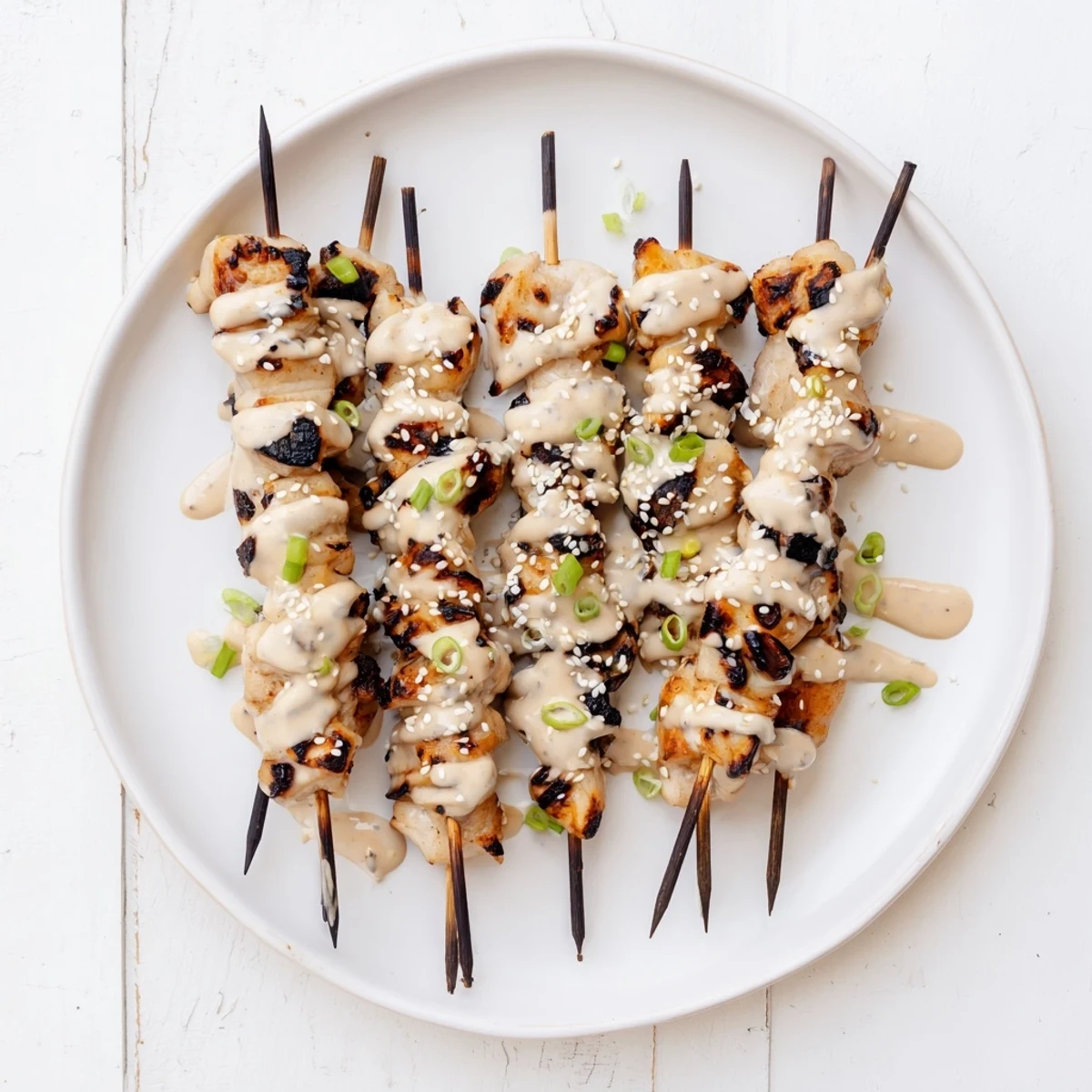 Golden grilled Bang Bang chicken skewers drizzled with creamy spicy sauce and sesame seeds
