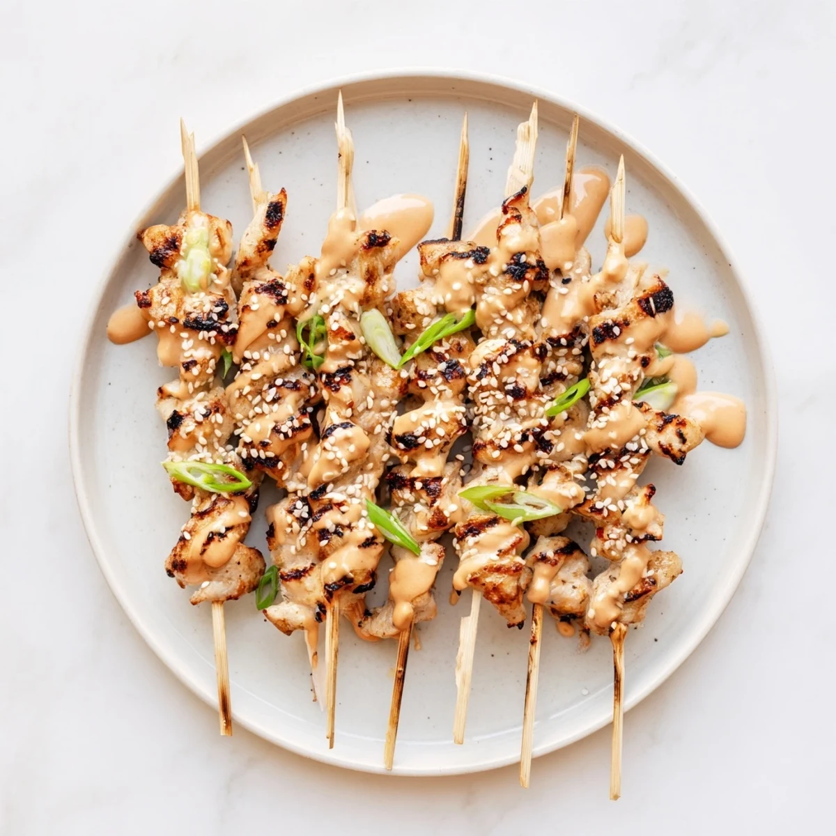 Tender Bang Bang chicken skewers on a platter garnished with sliced green onions