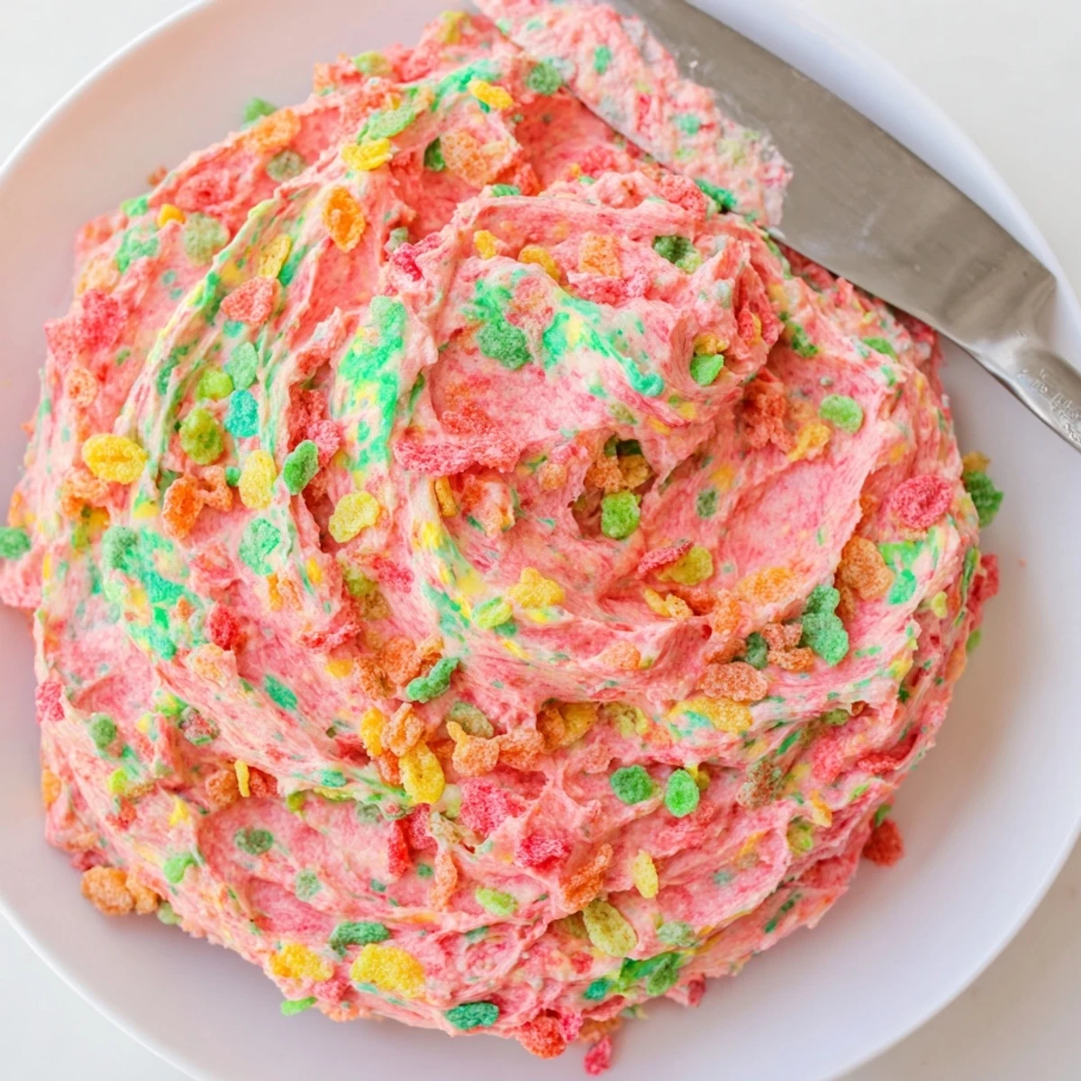 Fluffy rainbow speckled frosting studded with crushed Fruity Pebbles atop a freshly baked dessert