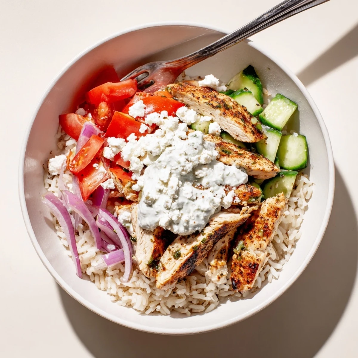 Delicious Greek Chicken Bowls served with rice, tomatoes, olives, and creamy tzatziki.
