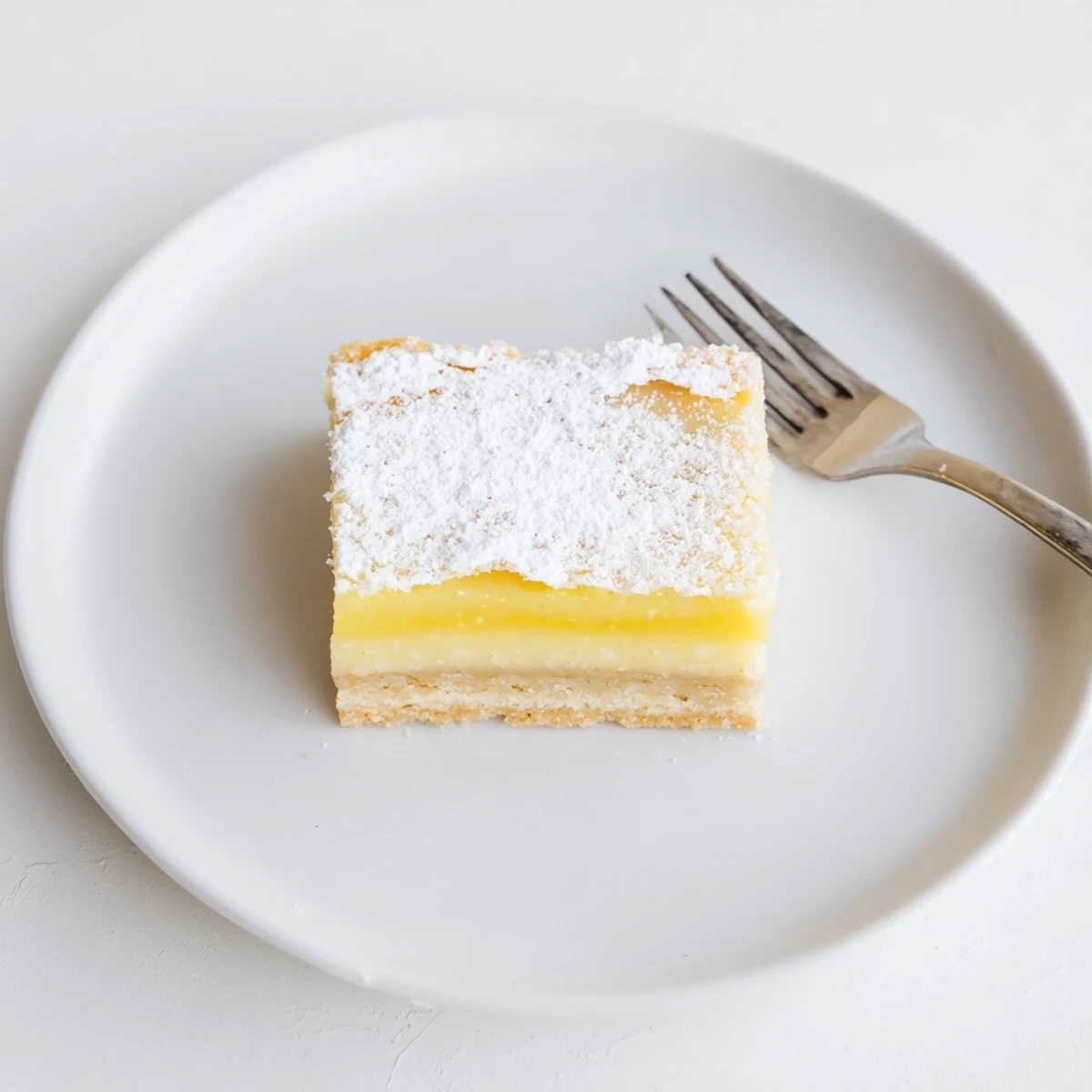 Golden simple lemon bars dusted with powdered sugar on a white plate.